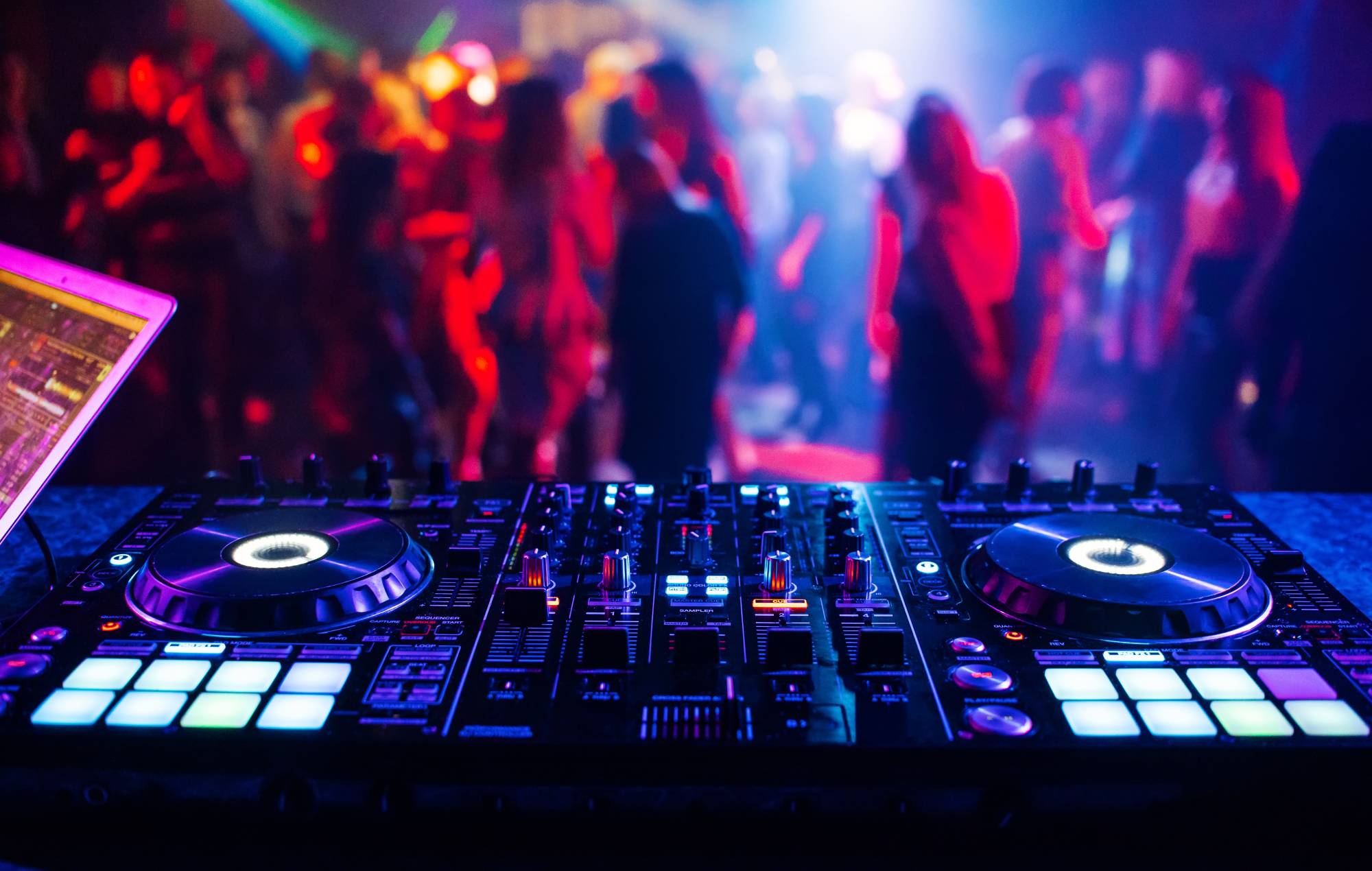 Music Controller DJ Mixer dans une boîte de nuit lors d'une fête en arrière-plan des silhouettes floues de la danse. Crédit Alex Koral via Getty
