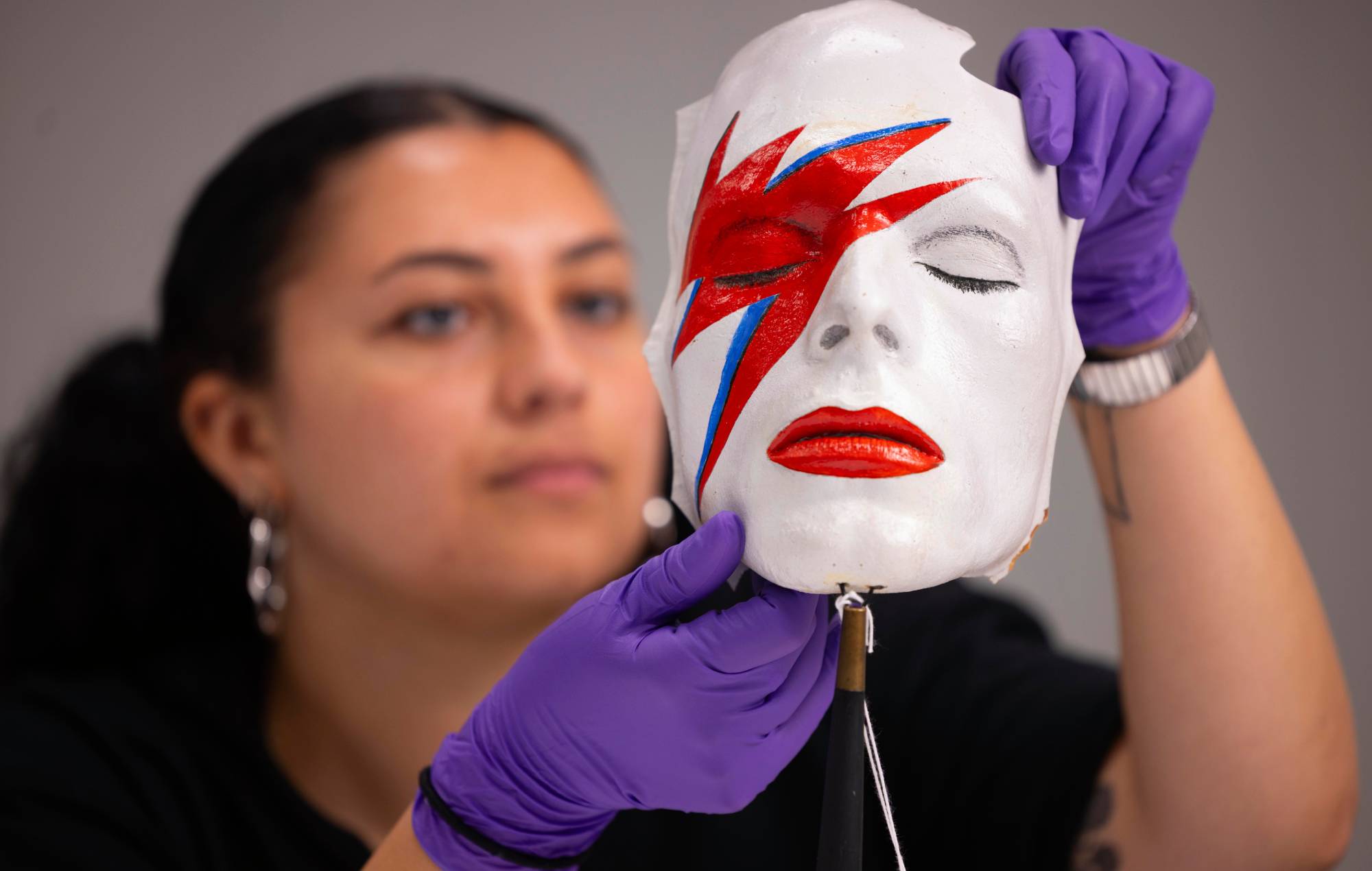 Un agent d'accès aux collections V&A gère un masque de vie de William Forsche du visage de David Bowie peint pour ressembler à son maquillage d'Aladdin Sane. Crédit: David Parry pour le V&A